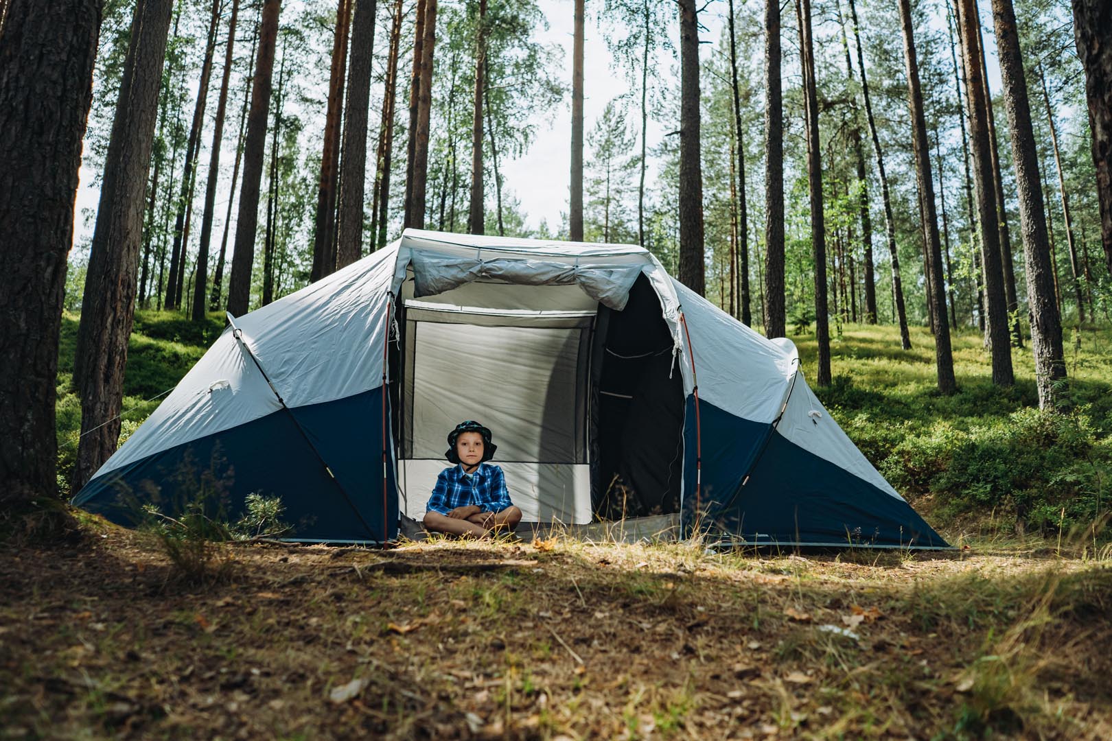 Cute caucasian boy wearing hat sitting inside big touristic tent family camping