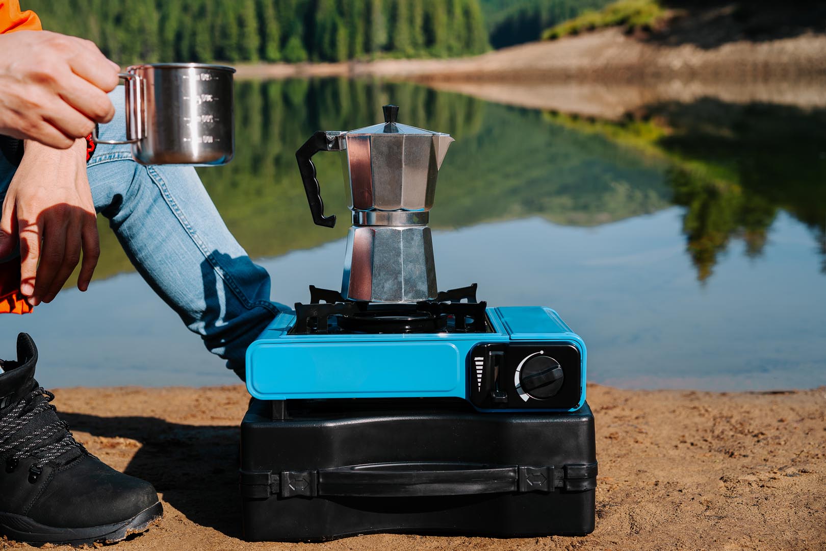 Man holding coffee cup by camping stove lake ahore
