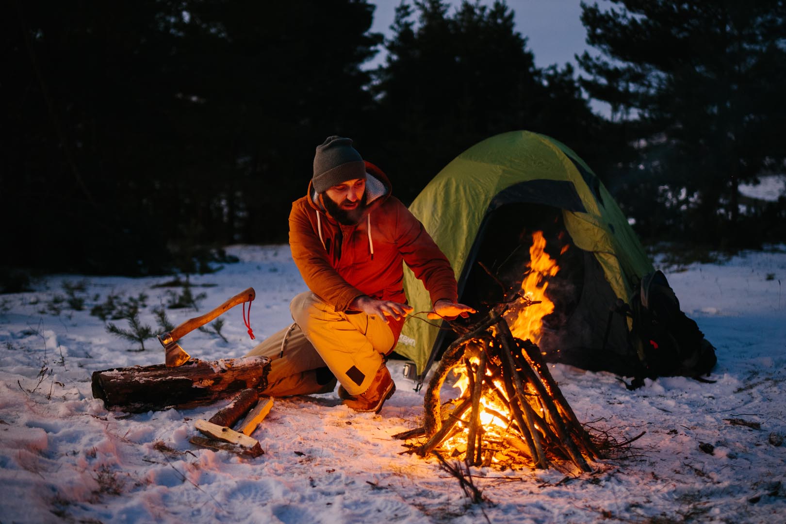Man sits near campfire warming himself by fire winter forest sunset