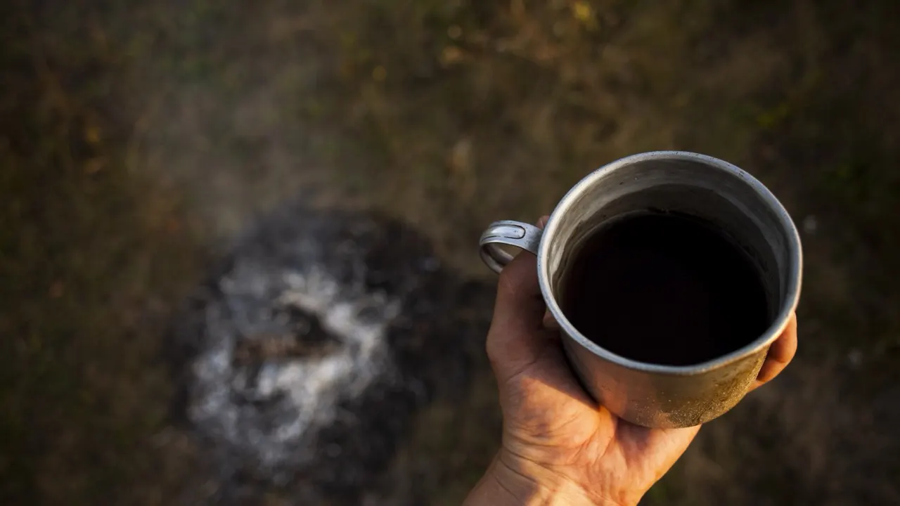 A mug of camp coffee beside a burned-out fire ring
